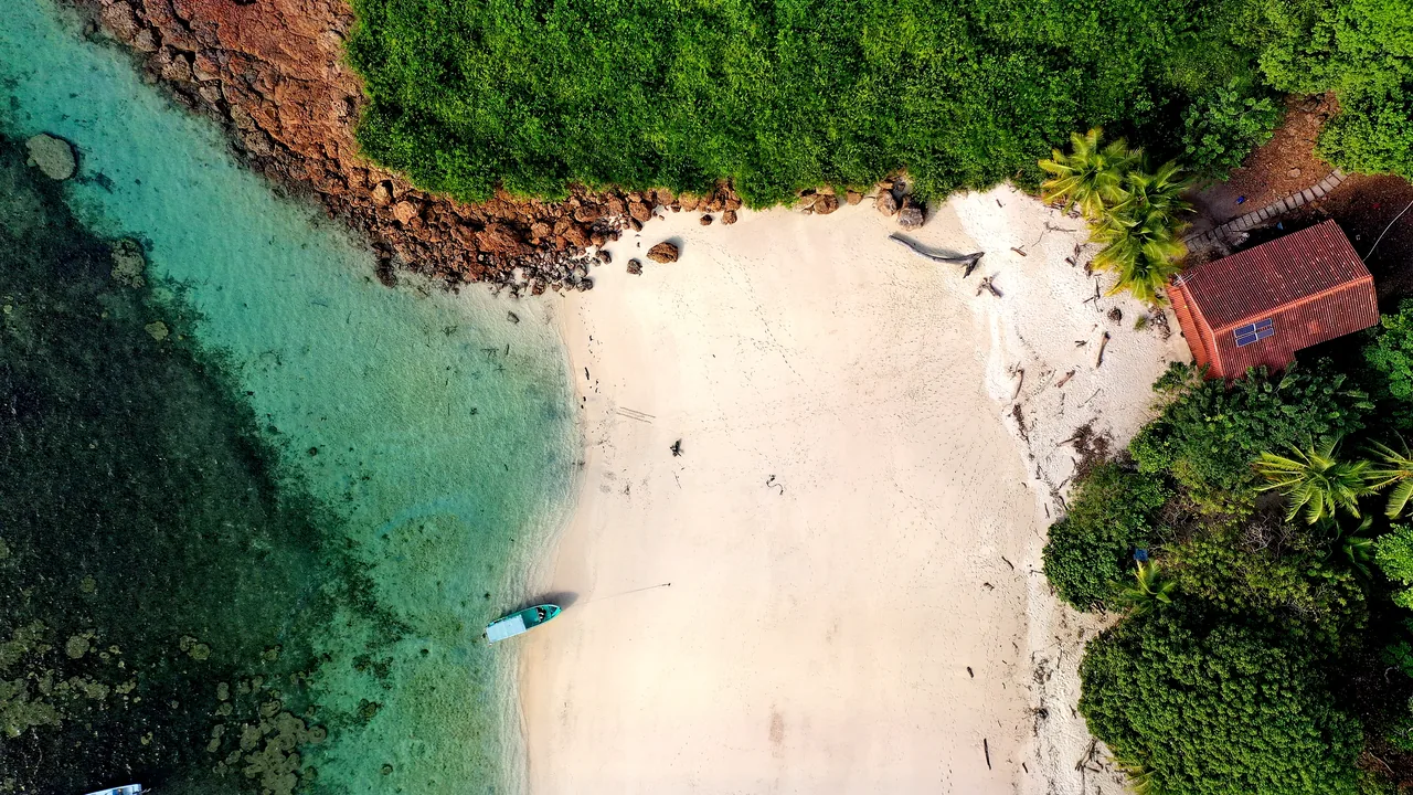 Aerial view of Isla Iguana: a white sand cove, a ranger station, and a panga at anchor in clear water.